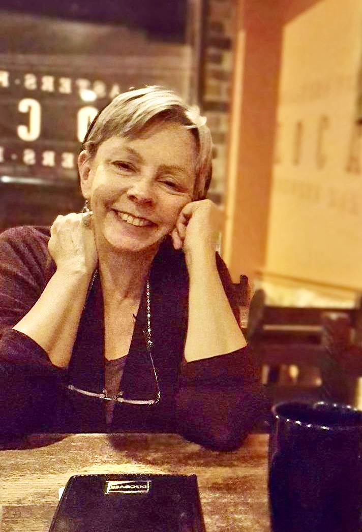 A white woman with short light hair smiling and sitting in a restaurant