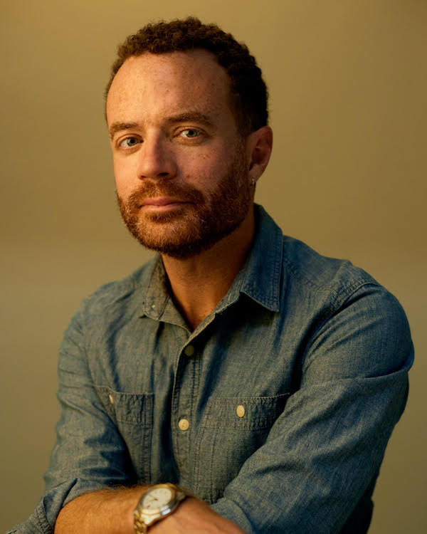 Portrait of a man with short brown hair and a short beard in a blue shirt looking at the camera